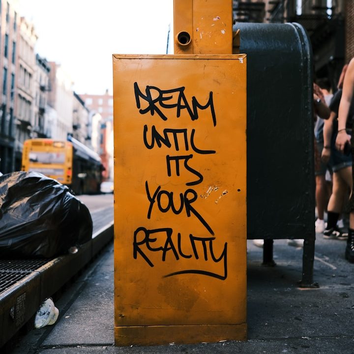 Marketing & Webdesign Graffiti mit der Aufschrift "Dream until it's your reality" auf einer gelben Wand.