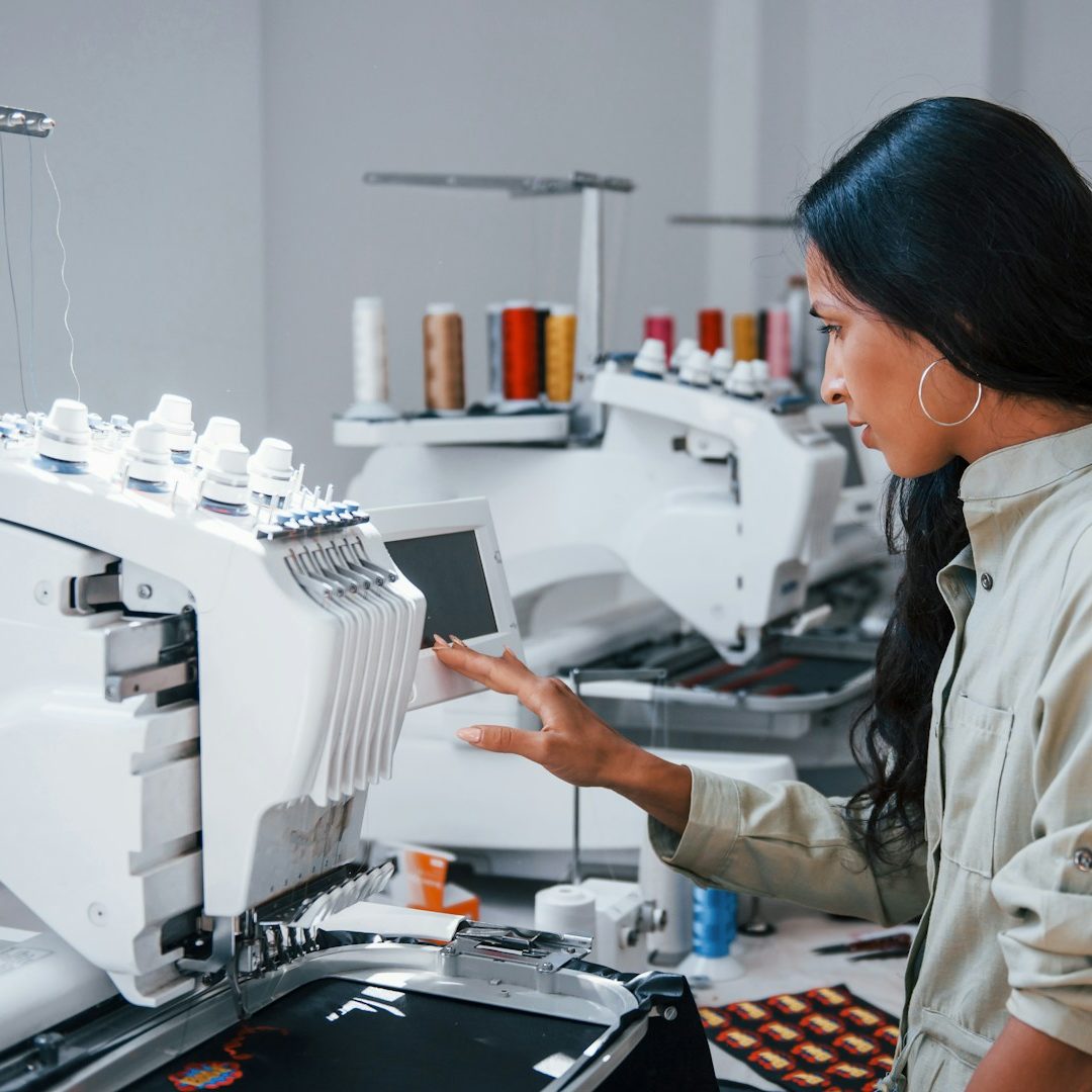 Bestickung & Textilveredelung Person arbeitet konzentriert an einer modernen Stickmaschine in einem hellen Raum.